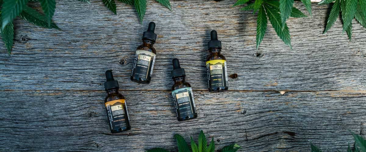 Four bottles of Charlotte's Web CBD Oil tinctures against a wood background.