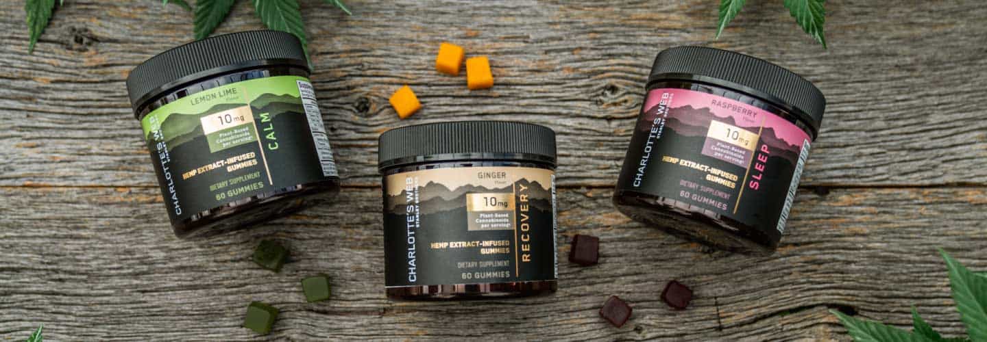 Three jars of Charlotte's Web CBD Gummies for Calm, Recovery, and Sleep against a wood surface.