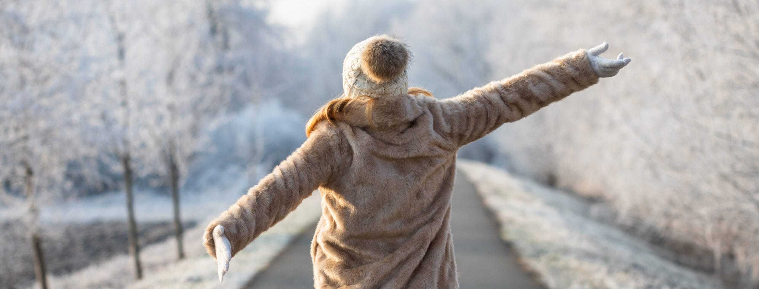 Person with arms outstretch in winter clothes on a snowy day.