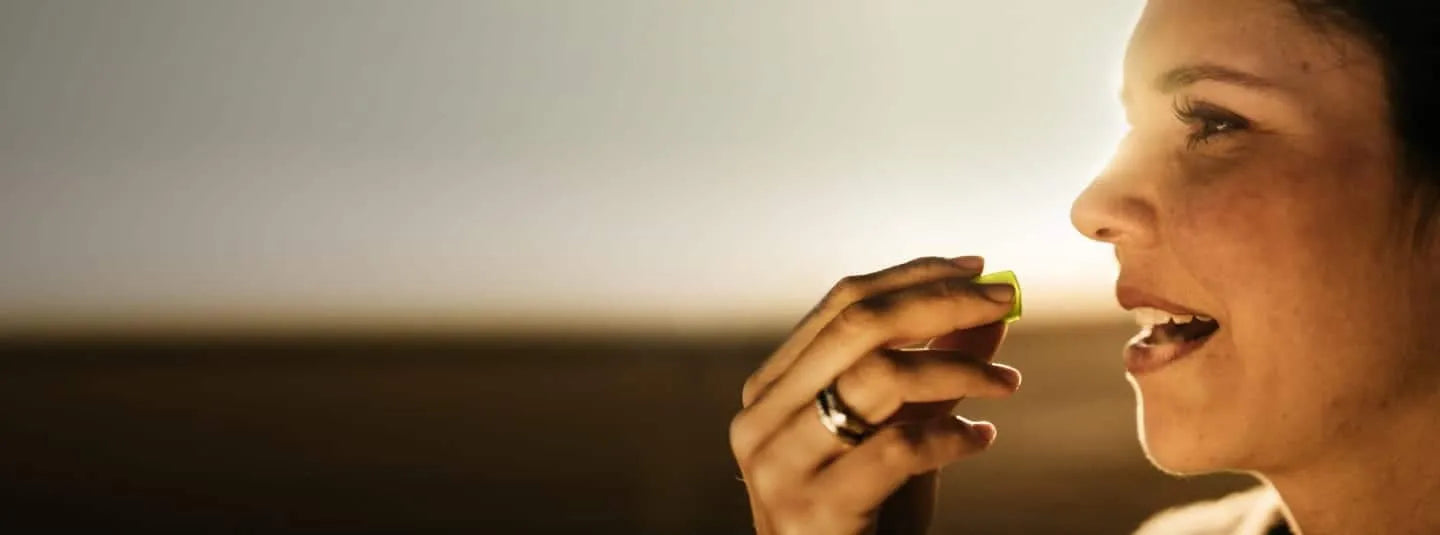 Profile of a woman putting a supplement in her mouth with the sun shining behind her.