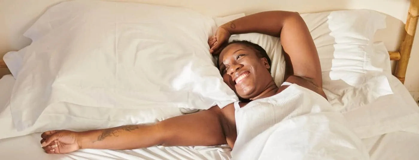 Happy woman waking up in bed with her arms stretched.