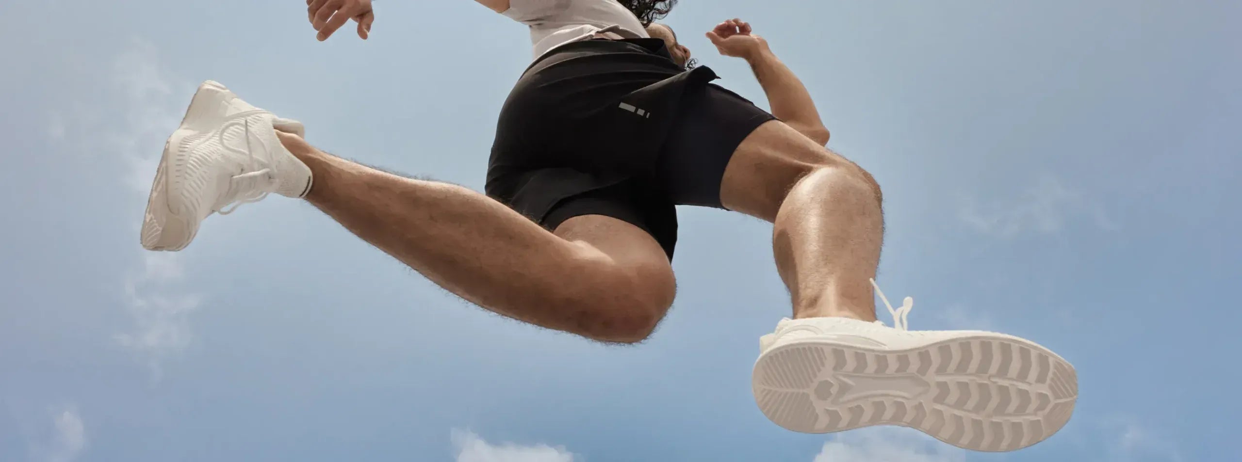 Image of a man jumping in the air, against a light blue sky.