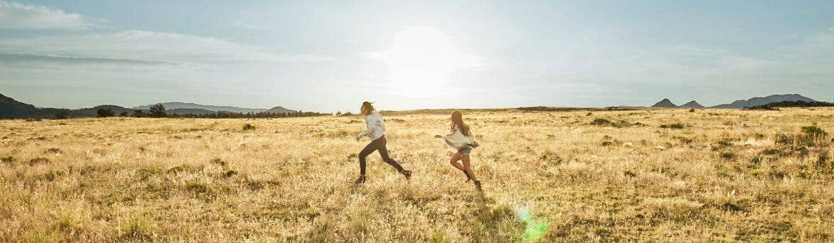 Two people running together in a field on a sunny day.