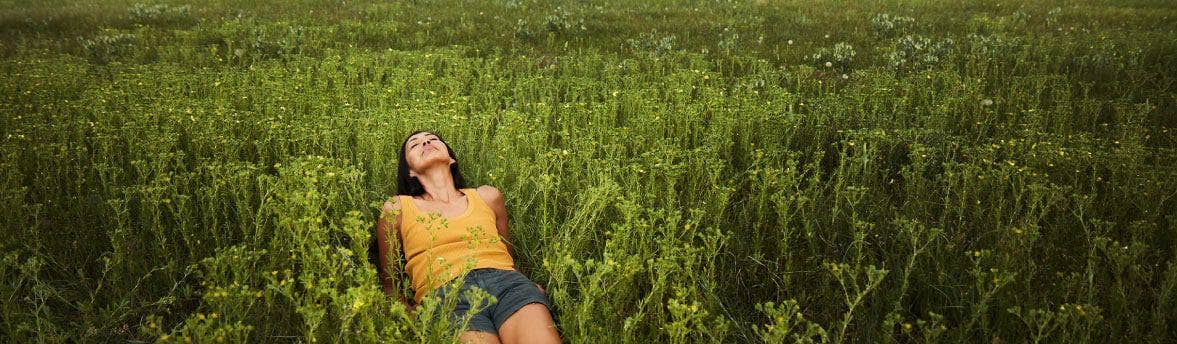 A woman laying in a tall grassy field enjoying the sun.