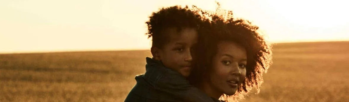A woman carrying her son on her back at dusk in a field.