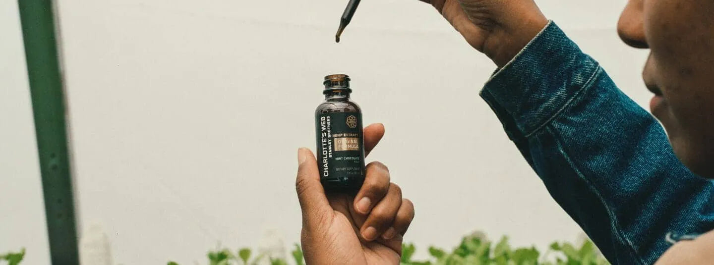 A person opening a bottle of Charlotte's Web CBD Oil tincture.
