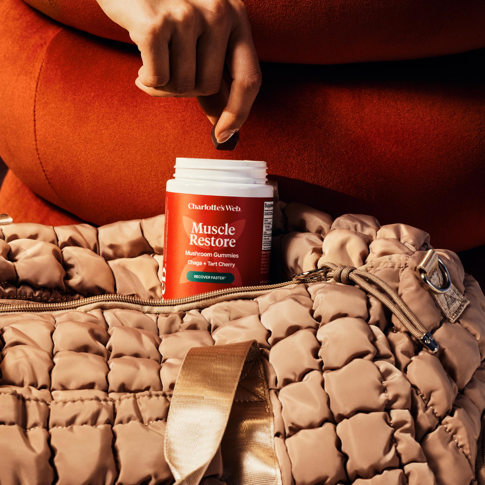 Hand reaching in a bottle of Muscle Restore gummies in a gym bag