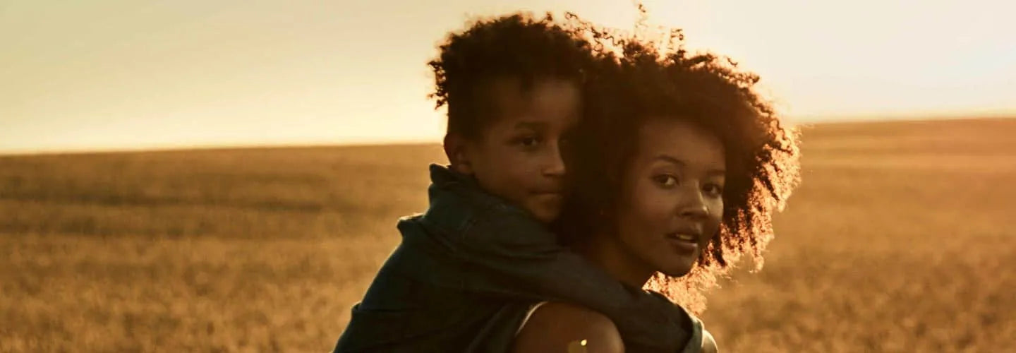 A mother carrying her son on her back at dusk.
