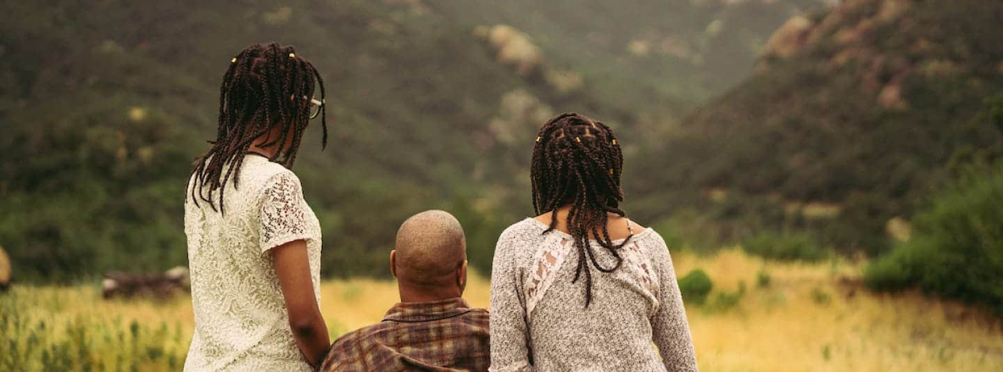 View of a father and his two daughters from behind, looking at nature.