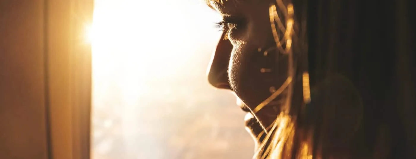 Profile of a woman looking out the window with the sun shining brightly.
