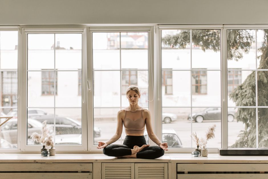 Woman meditating in lotus pose near large window