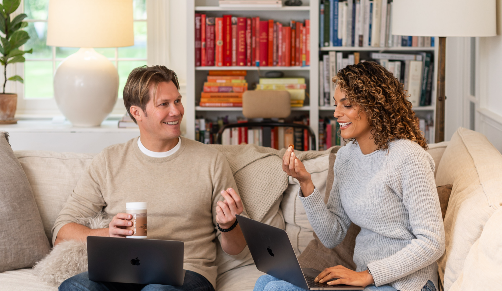 Man and woman working on laptops in a cozy living room, enjoying Charlotte's Web™ Focus Support gummies. 