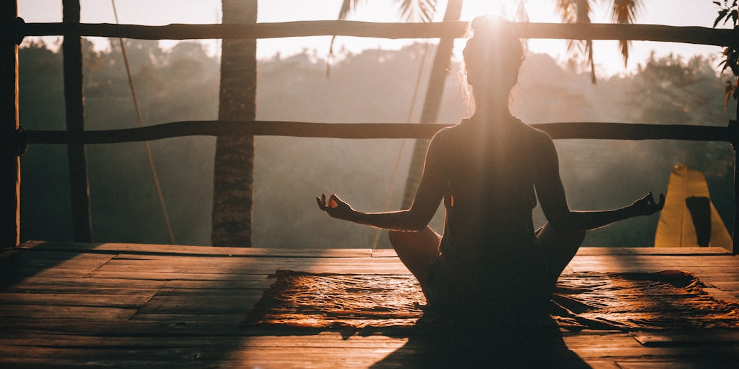 Person meditating outdoors at sunrise with palm trees