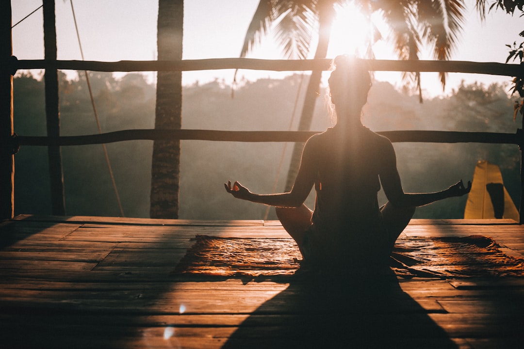Person meditating outdoors at sunrise with palm trees