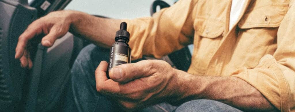 A person's hands holding Charlotte's Web CBD Oil in a yellow shirt.