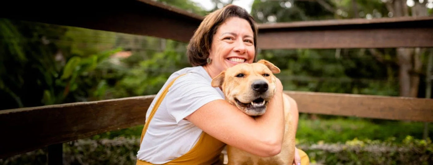 Woman smiling while hugging happy dog outdoors near wooden fence
