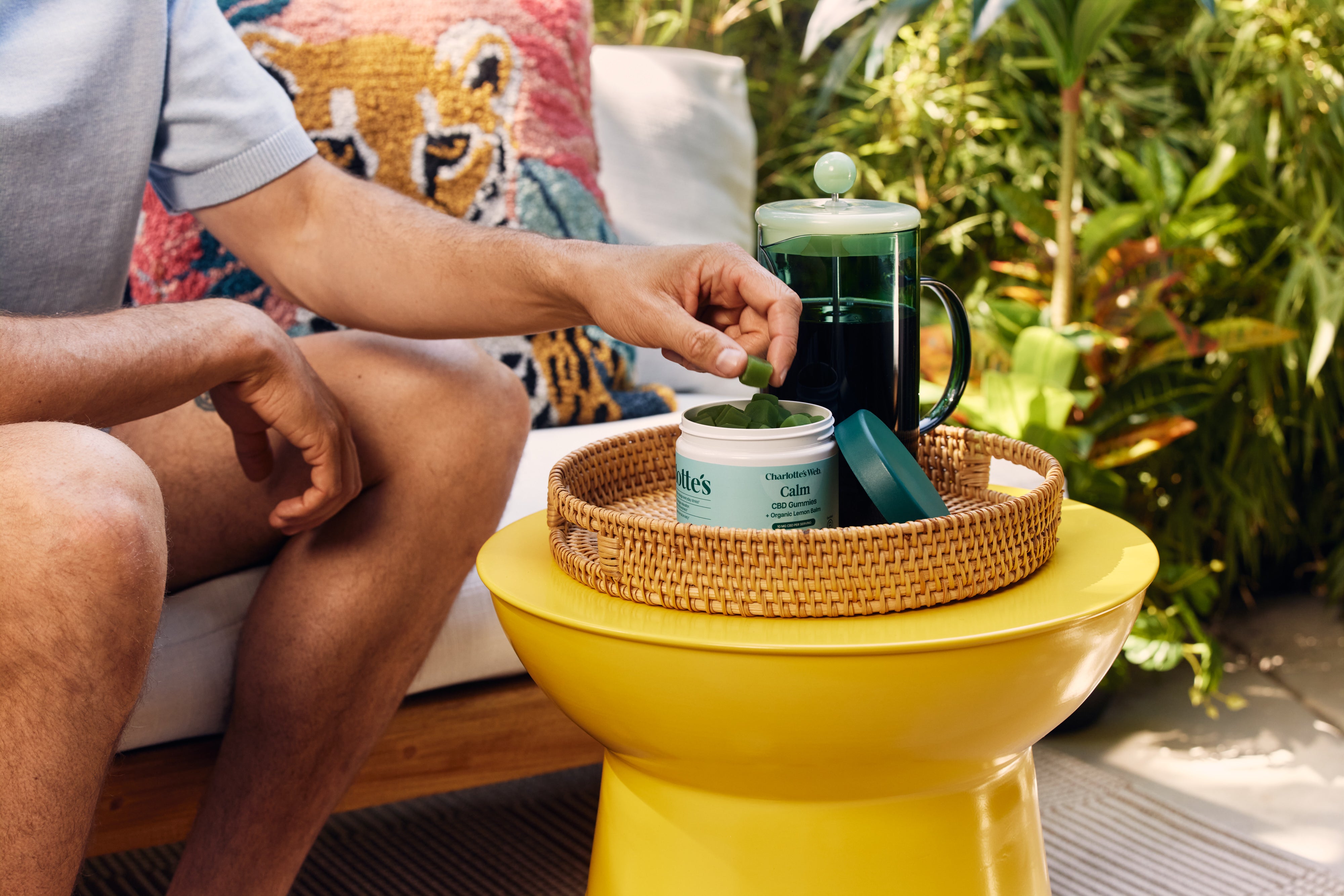 Person sitting on a couch with a yellow side table, holding a green leaf over a container.