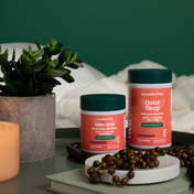 Product Image for Two containers of Charlotte&#39;s Web Quiet Sleep supplement on a table with a plant and candle in the background.