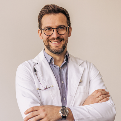 Man wearing a white lab coat with arms crossed against a plain background
