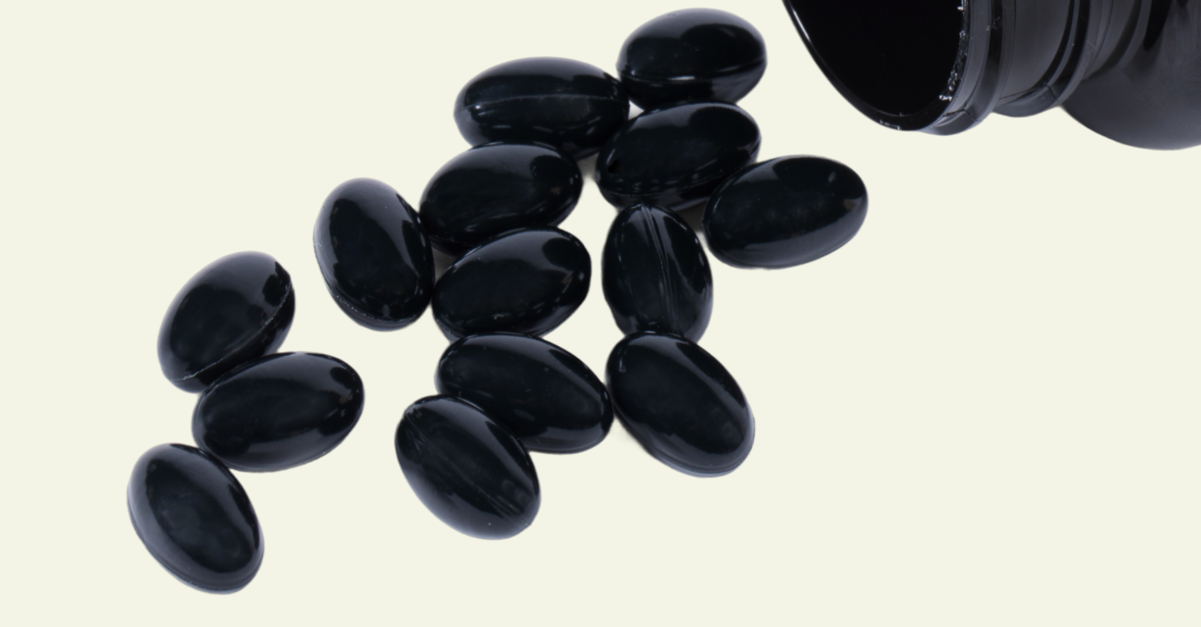 Black pills spilling out of a black container on a light beige background