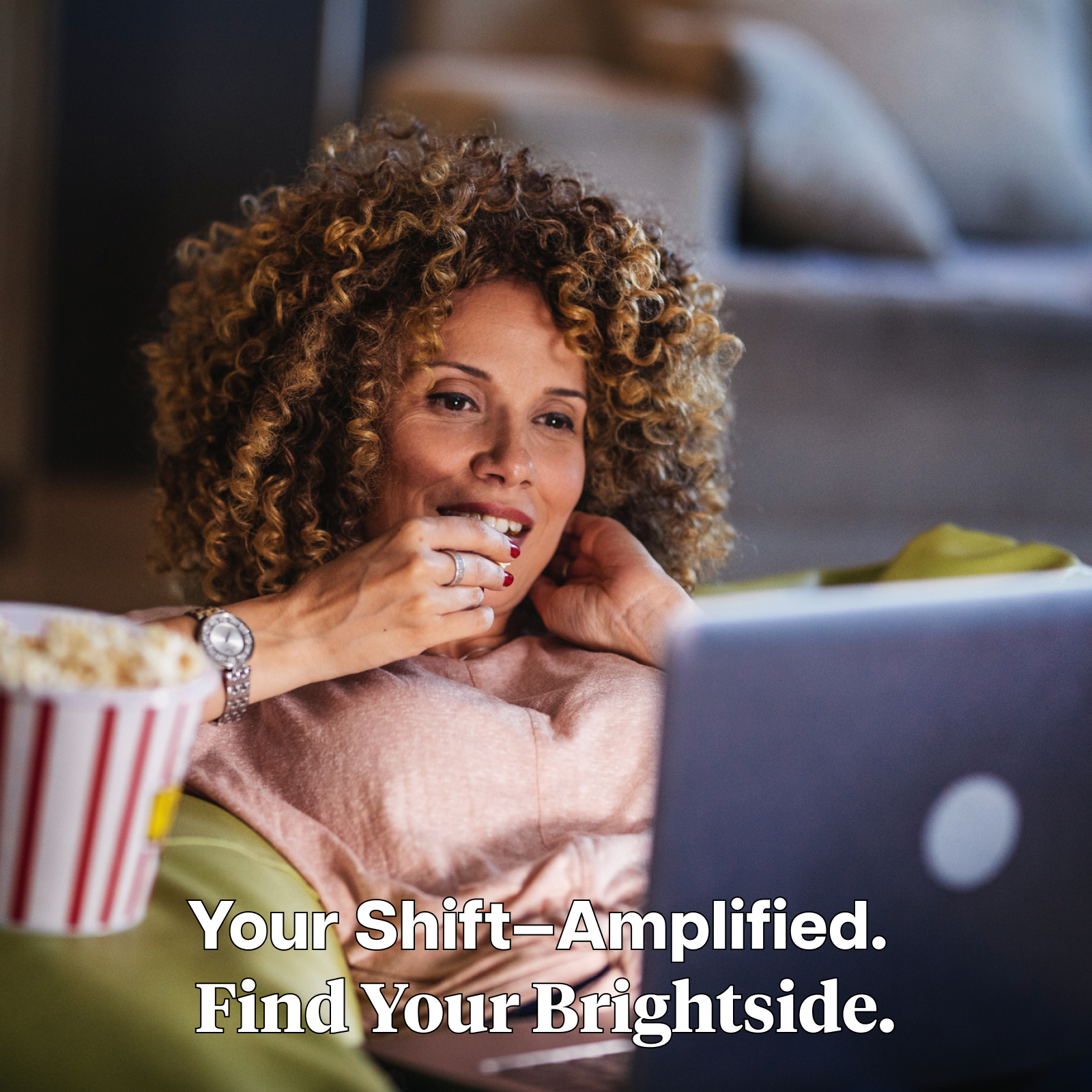 Product Image for Woman sitting on a couch, watching a laptop screen eating popcorn with text 'Your Shift — Amplified. Find Your Brightside.'