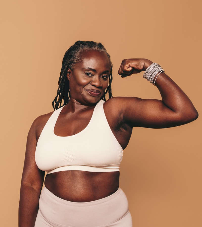 Woman flexing her arm muscles against a beige background