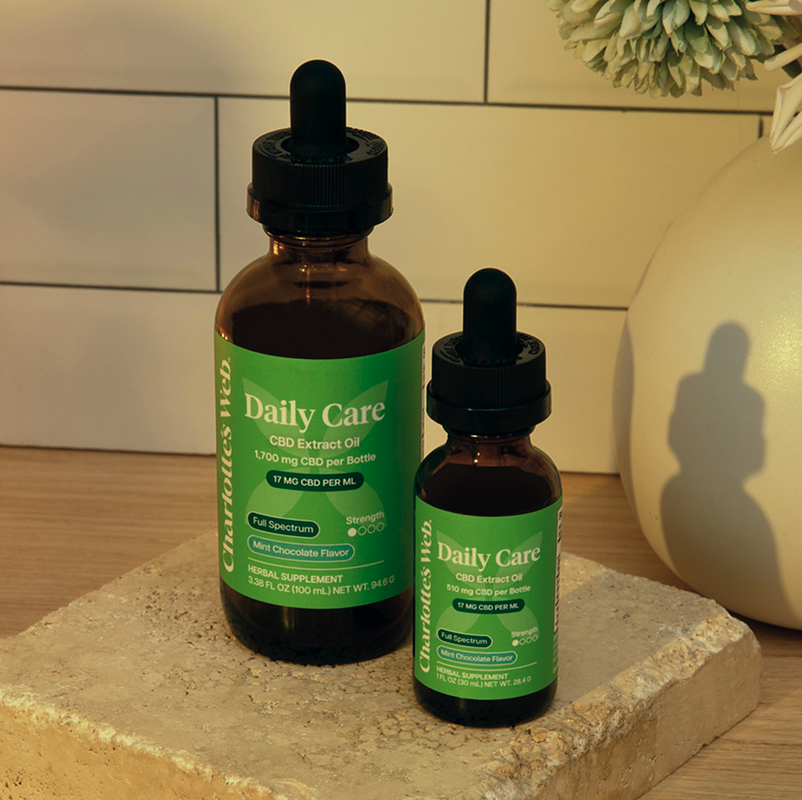 Two amber glass dropper bottles with green labels, one larger and one smaller, displayed on a stone slab next to a beige ceramic vase on a tiled surface.