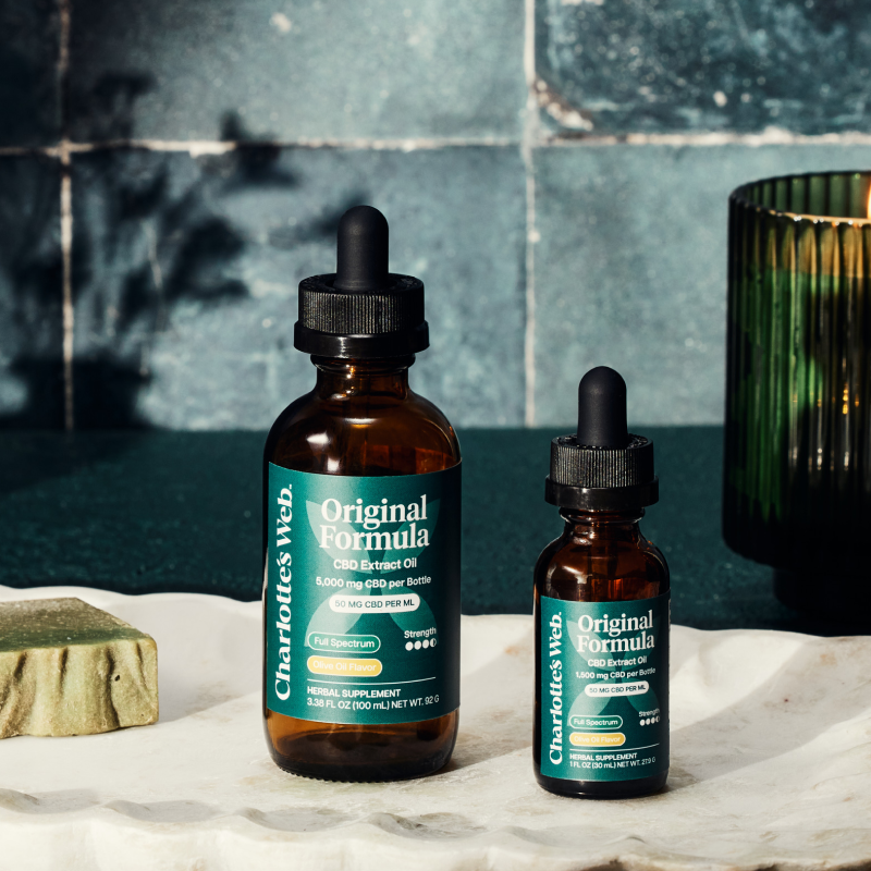 Product Image for Two bottles of Charlotte's Web Original Formula CBD Extract Oil on a marble surface with a tiled wall background.
