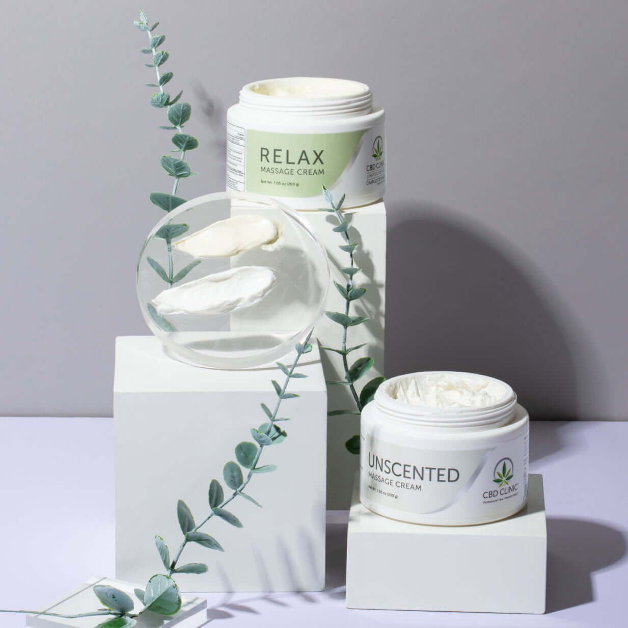 Two jars of massage cream labeled 'Relax' and 'Unscented' with eucalyptus leaves on a gray background.